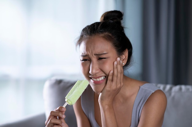 La giovane donna asiatica ha denti sensibili con il ghiaccio la donna che mangia il gelato ha mal di denti concetto di assistenza sanitaria