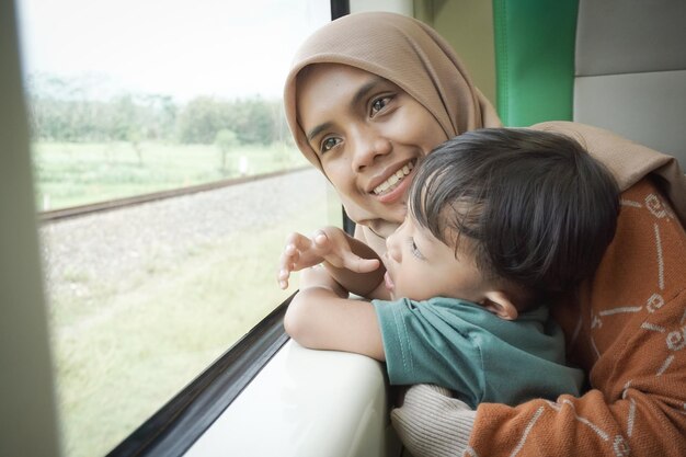 ヒジャブを着た若いアジア人女性と幸せな息子が電車内で冗談を言いながら窓の外を眺めている