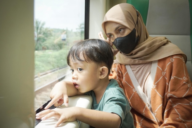 Young asian woman in hijab and her son are talking and looking out the window inside the train