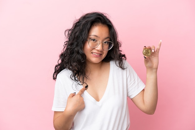 Young asian woman holding a Bitcoin isolated on pink background with surprise facial expression