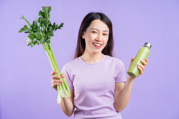 보라색 배경에 주스 한 병을 들고 있는 젊은 아시아 여성