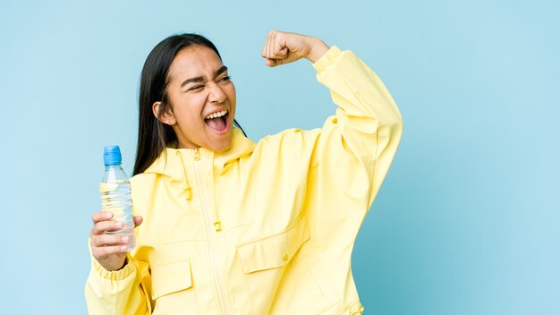 Young asian woman holding a bottle of water raising fist after a victory, winner concept.