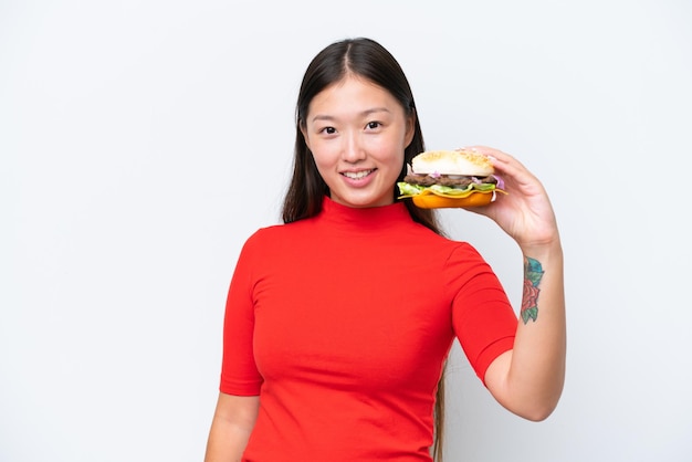 Photo young asian woman holding a burger isolated on white background with happy expression