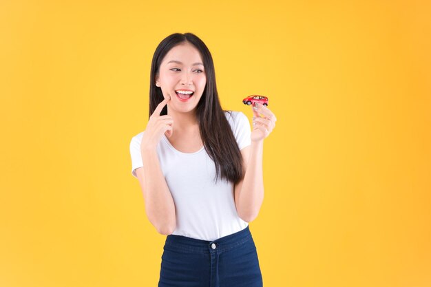 Young asian woman holding car model and showing mini heart sign\
isolated on white background travel insurance concept