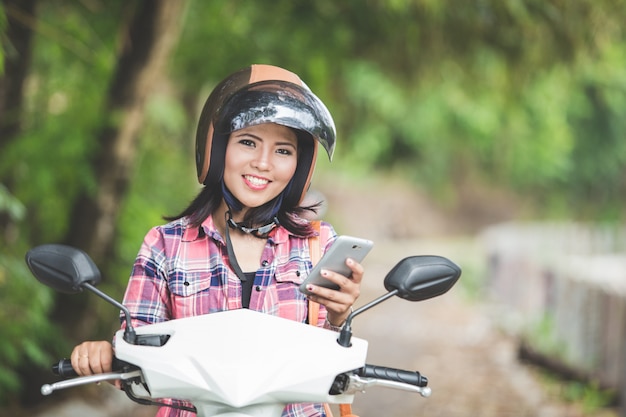 Giovane donna asiatica che tiene un cellulare mentre sedendosi su un motorcy