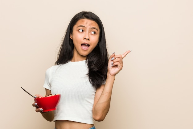 Young asian woman holding a cereals bowl pointing to the side