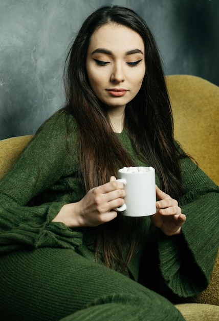 Young asian woman holding coffee cup and sitting on chair at home