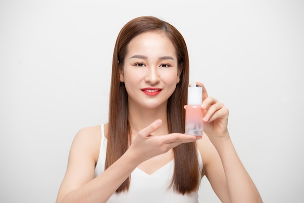 Молодая азиатка держит бутылку косметического продукта на белом фоне