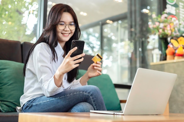 Young Asian woman holding credit card and mobile phone for electronic payment in internet online remote store