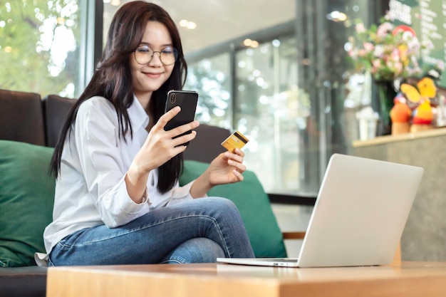 Young Asian woman holding credit card and mobile phone for electronic payment in internet online remote store