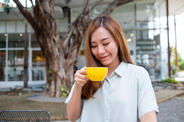 コーヒーを持って飲んでいる若いアジア人女性