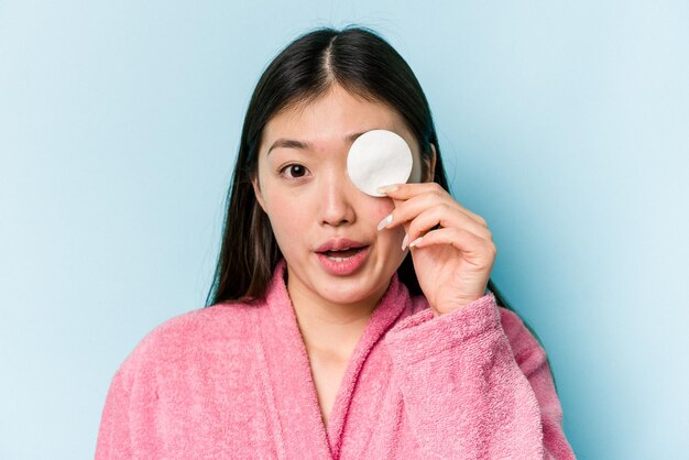 Young asian woman holding a facial disk isolated on pink background