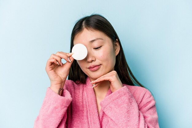 Young asian woman holding a facial disk isolated on pink background