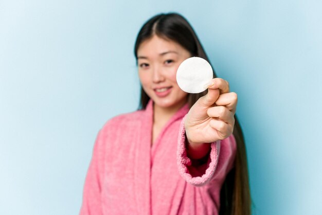 ピンクの背景で隔離の顔のディスクを保持している若いアジアの女性