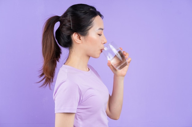 young asian woman holding glass of water on purple background