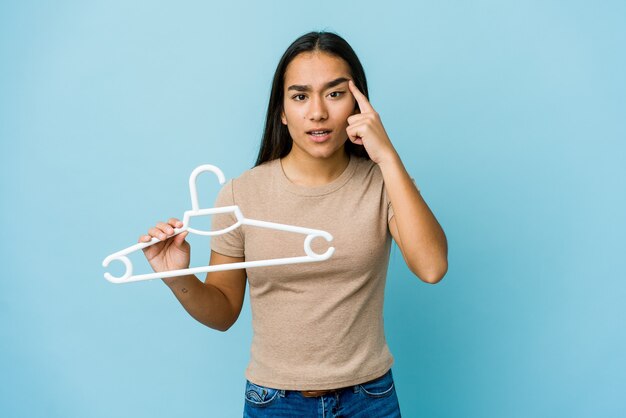 Young asian woman holding a hanger showing a disappointment gesture with forefinger.