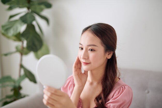 Young Asian woman holding and looking in the mirror at living room