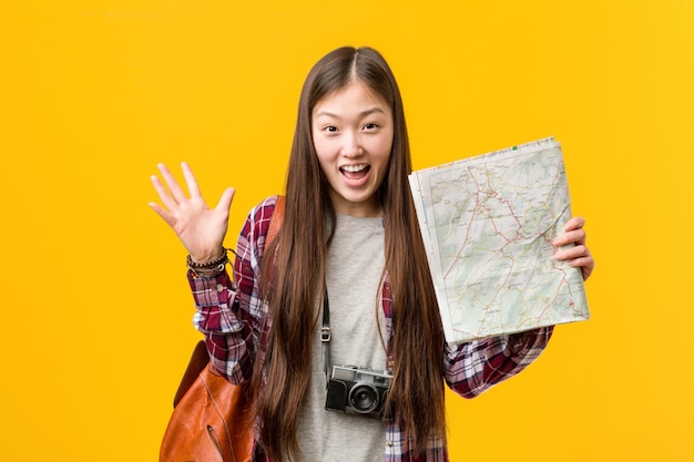 Young asian woman holding a map celebrating a victory or success