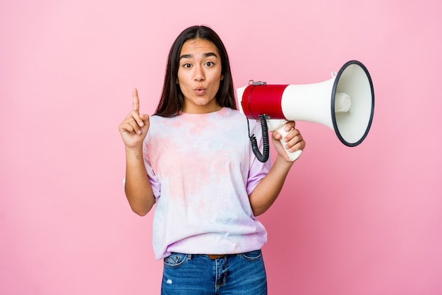 Giovane donna asiatica che tiene un megafono isolato sulla parete rosa che ha qualche grande idea, concetto di creatività.