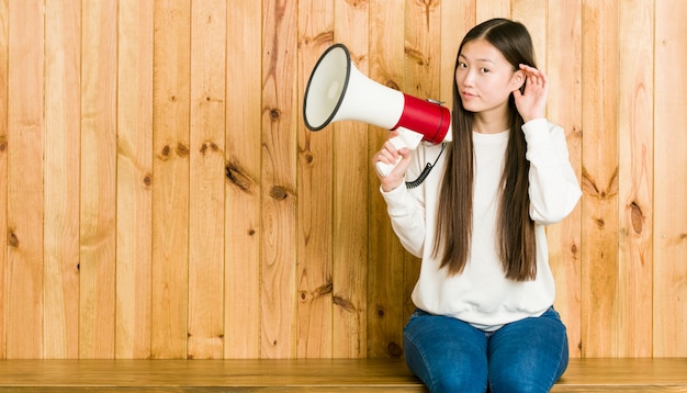 Giovane donna asiatica che tiene un megafono che prova ad ascoltare un gossip.