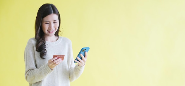 온라인 쇼핑을 위해 휴대전화와 신용카드를 들고 있는 젊은 아시아 여성