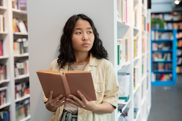 図書館で開いた本を保持している若いアジアの女性