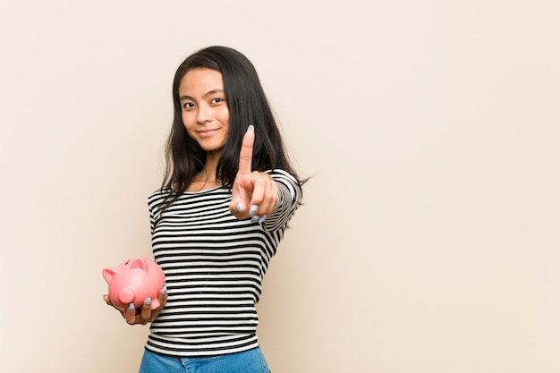 指でナンバーワンを示す貯金を保持している若いアジア女性。