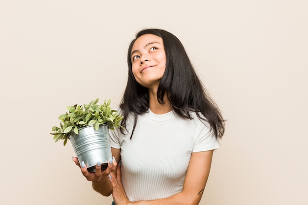 Young asian woman holding a plant laughing and having fun.