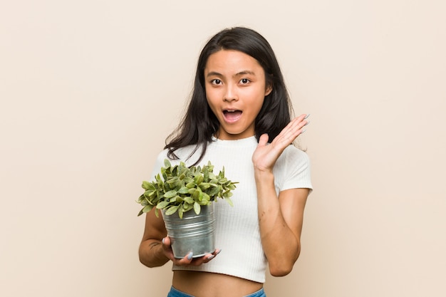 驚いたとショックを受けた植物を保持している若いアジア女性。
