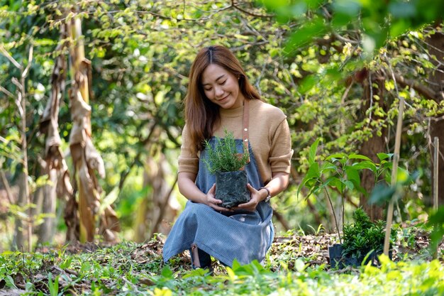 家の園芸の概念のためにローズマリーの木を植える準備をしている若いアジアの女性