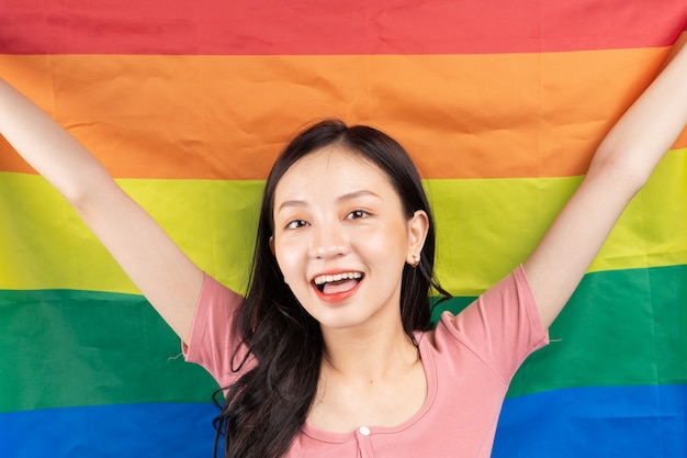 Young asian woman holding rainbow flag to support lgbtq+\
community on blue