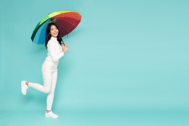 Молодая азиатская женщина, держащая радужную зонтик стоя изолирована на зеленом фоне, все тело