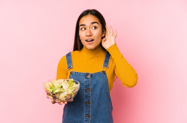 Young asian woman holding a salad trying to listen a gossip.