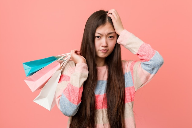 ショックを受けている買い物袋を保持している若いアジア女性、彼女は重要な会議を覚えています。