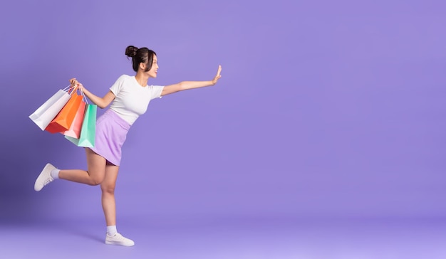 Young asian woman holding shopping bag on purple background