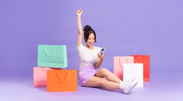 Young Asian woman holding shopping bag on purple background