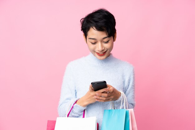 Young Asian woman holding shopping bags and writing a message with her cell phone to a friend