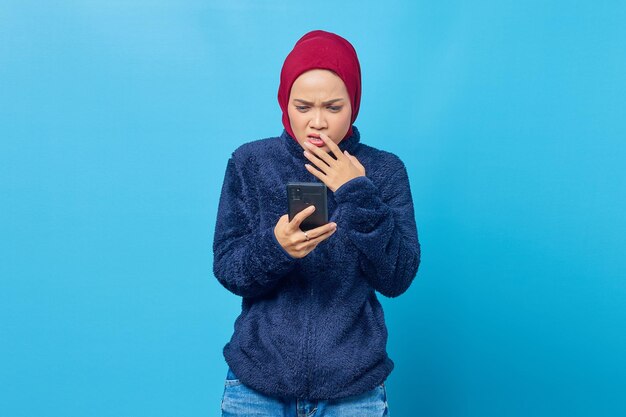 Young Asian woman holding smartphone looks anxious and worried afraid of something