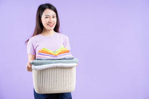 Young Asian woman holding a stack of clothes on purple background