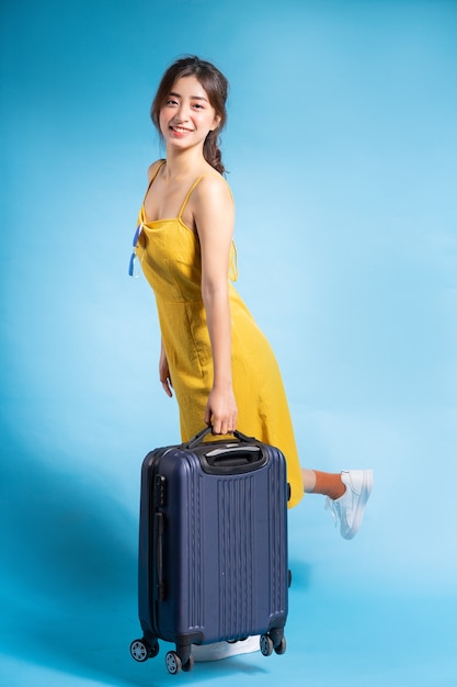 Young Asian woman holding suitcase on blue, summer concept