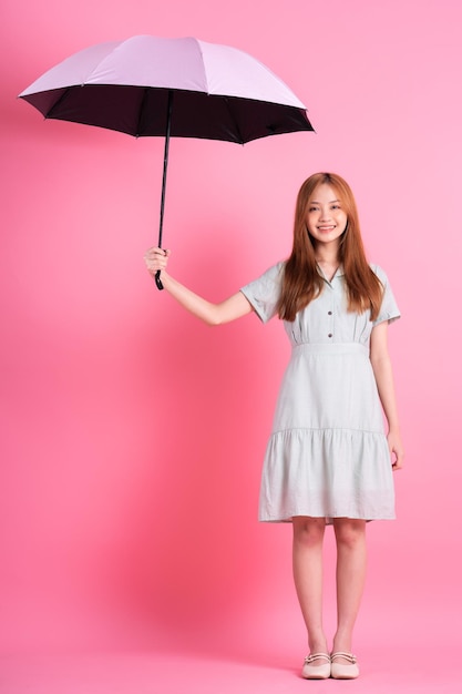 Young Asian woman holding umbrella on pink background