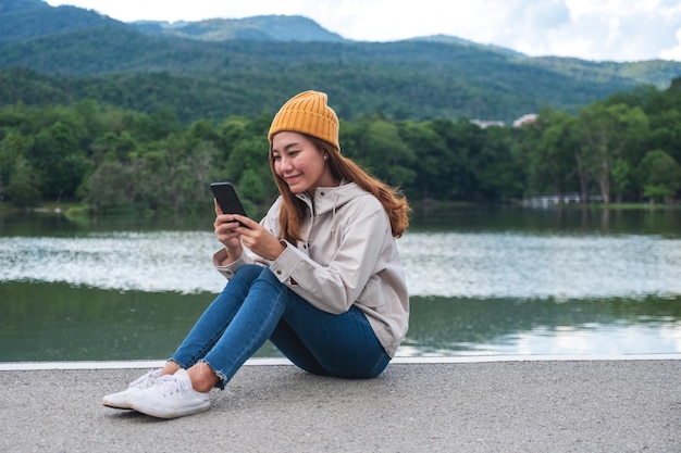 山や湖を旅行中に携帯電話を持って使用している若いアジアの女性