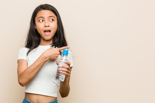 Young asian woman holding a water bottle pointing to the side