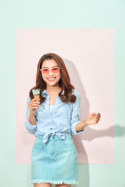 Young asian woman holds tasty ice cream, stands on light pink background