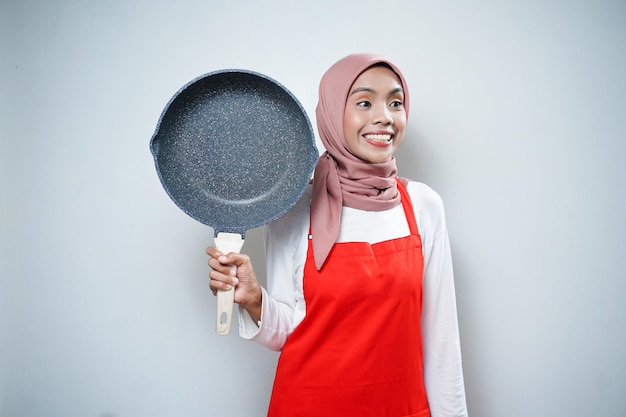 Молодая азиатская домохозяйка в кухонном фартуке готовит и держит сковороду