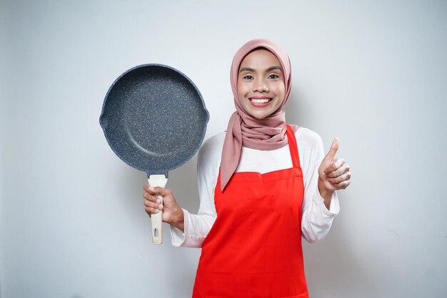 Young Asian woman housewife wearing kitchen apron cooking and holding pan