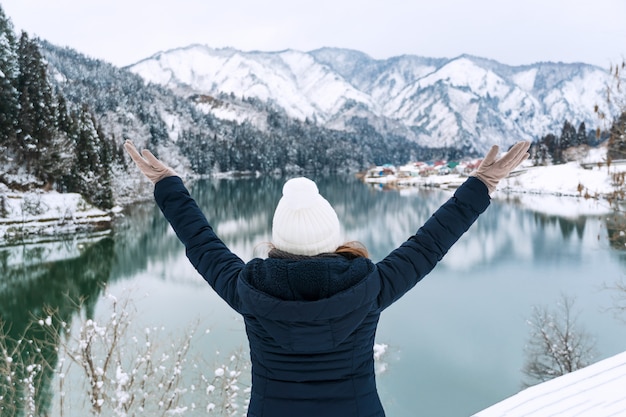 写真 冬のコートを着た若いアジア女性は雪に覆われた山の風景でリラックスします。