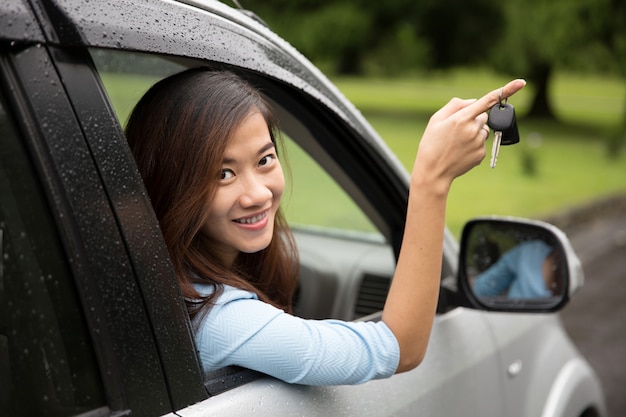 車の中の若いアジア女性が窓からキーを押したままにします