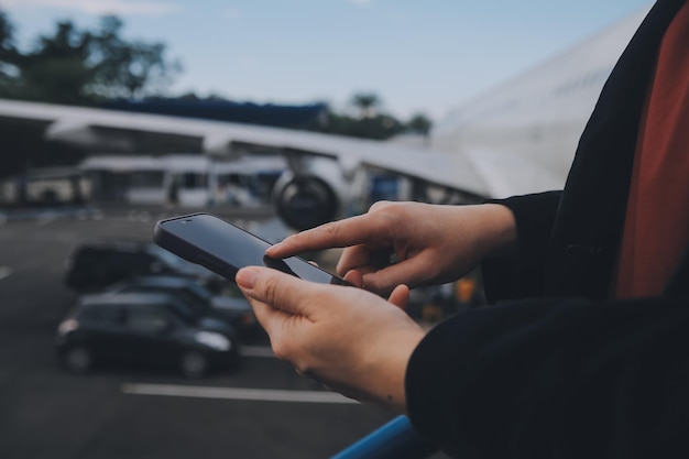 Foto giovane donna asiatica in un aeroporto internazionale che usa uno smartphone mobile e controlla il volo alla scheda di informazioni sul volo