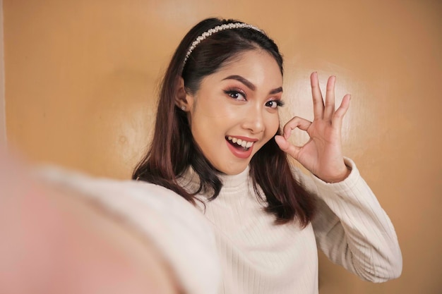 Young Asian woman is selfie with happy smiling face and ok sign on near of mouth look at the camera